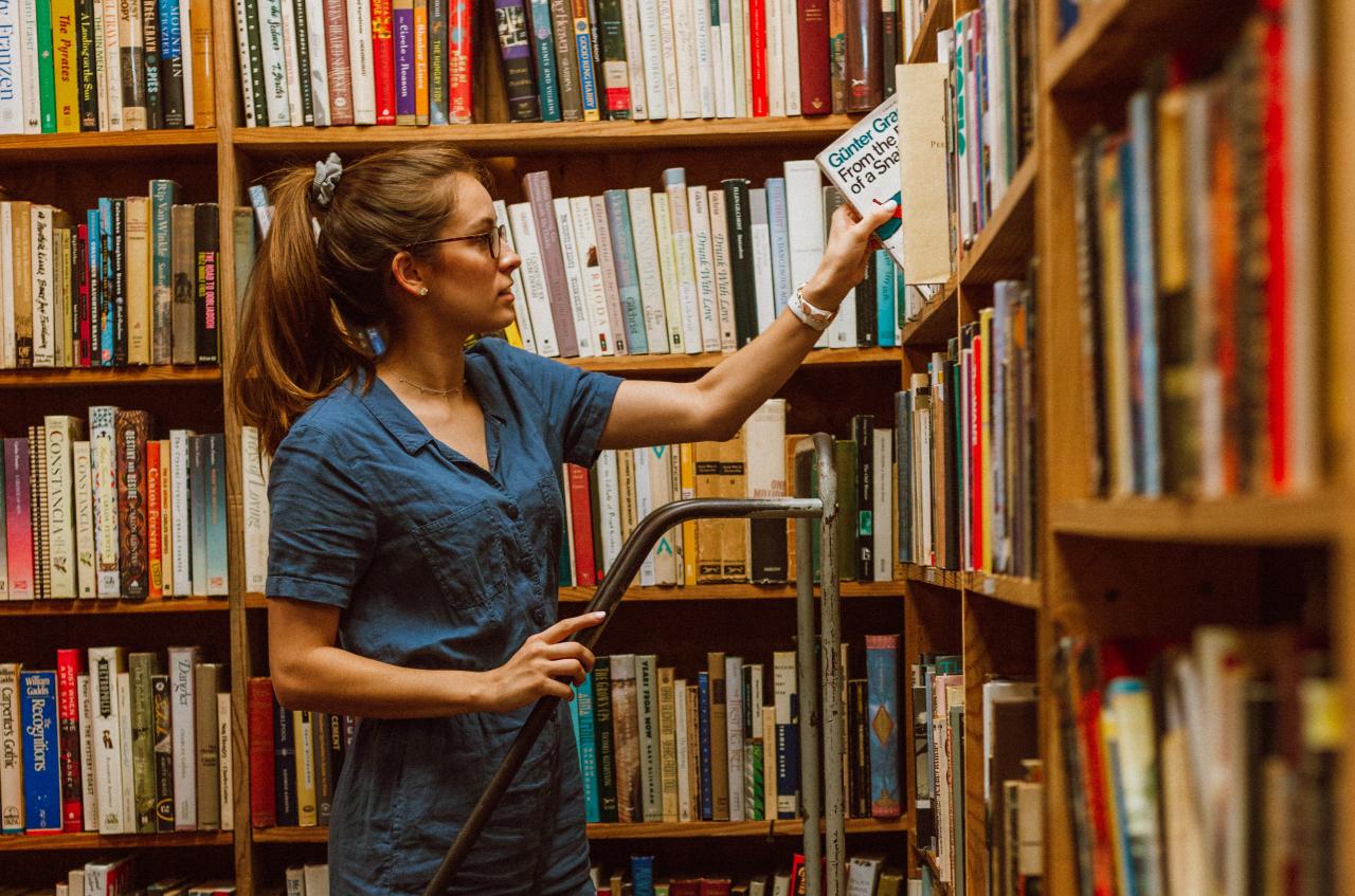 Junge Frau auf einer Leiter vor dem Bücherregal